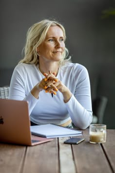 a woman sitting at a wooden table with a laptop computer in front of her and a glass of orange juice