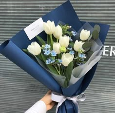 a bouquet of white tulips wrapped in blue paper and tied with a ribbon