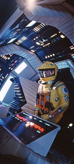 a man in a yellow space suit and helmet standing next to a sci - fi machine