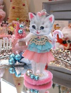 a white cat figurine wearing a pink and blue dress on top of a table