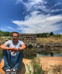 a man sitting on top of a rock next to a pond with water in it