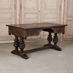 an old wooden table with two turned legs and carvings on the top, sitting in front of large doors