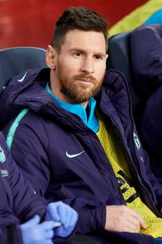 a man with a beard sitting on a bench wearing blue gloves and a purple jacket