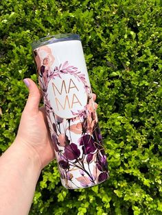 a person holding up a tumbler cup in front of some bushes and plants with the word ma on it