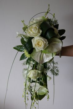 a bouquet of white roses and greenery is being held by someone's hand