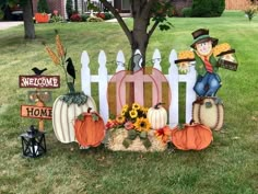 pumpkins and scarecrows are sitting in front of a white picket fence