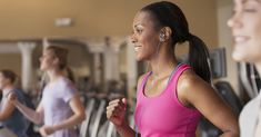 a woman running on a treadmill with ear buds in her ears and headphones around her neck