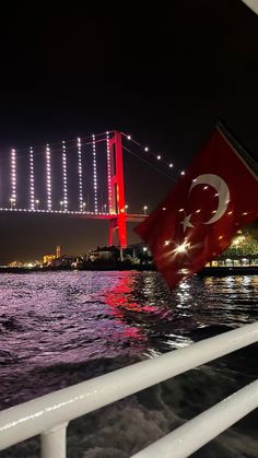 there is a flag on the side of a boat in the water near a bridge