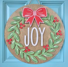 a christmas wreath with the word joy painted on it and a bow hanging from the front door