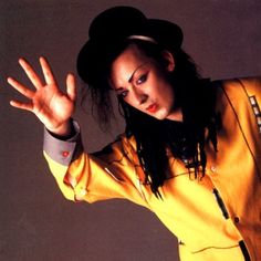 a woman wearing a yellow jacket and hat with her hands in the air while posing for a photo