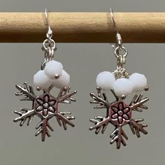 snowflake earrings with white beads hanging from a wooden stick on a gray background