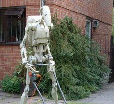 a robot is standing in front of a brick building with a power drill attached to it