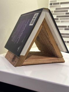 an open book sitting on top of a wooden stand with a white wall in the background