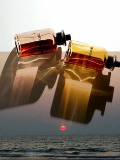 two empty bottles sitting on top of each other in front of the ocean and sun