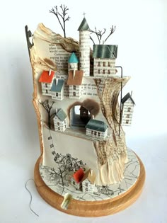 a ceramic model of a castle with trees and buildings on it's sides, sitting on a wooden base