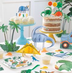 a table topped with cake and cupcakes covered in paper dinosaurs on top of plates