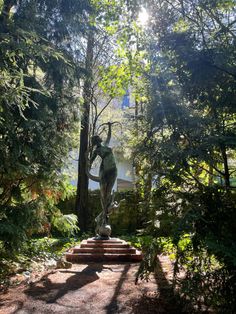 a statue in the middle of a garden surrounded by trees and bushes with sunlight shining through the leaves