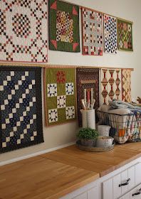 several quilts are hanging on the wall above a counter in a room with white cabinets and drawers