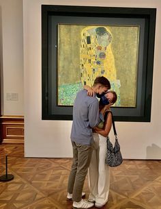 a man and woman kissing in front of a painting on display at an art museum