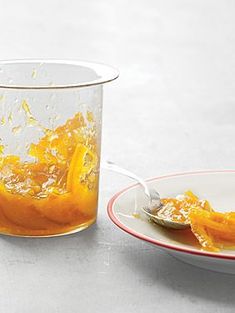 a glass filled with orange juice next to a bowl full of orange peels and a spoon