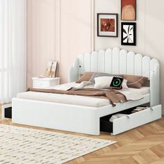 a white bed with drawers underneath it in a room that has pink walls and hardwood floors