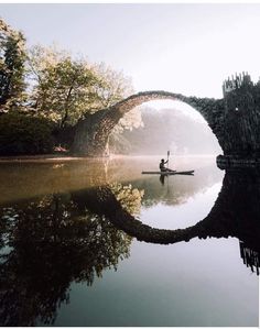 a person in a kayak on the water under a bridge with trees around it