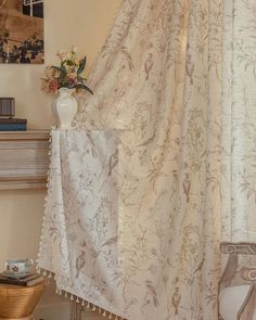 a white vase sitting on top of a table next to a window covered in curtains