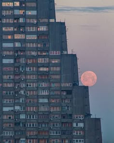 the moon is setting in front of an apartment building with windows and balconies