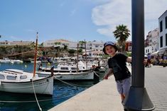 a young boy standing on the dock next to boats