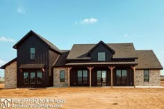 a large black house sitting in the middle of a dirt field with lots of windows