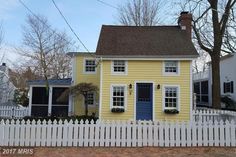 a yellow house with white picket fence and trees