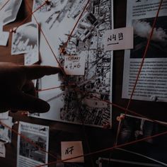 a person pointing at pictures on a wall with red string attached to it and pinned to the wall