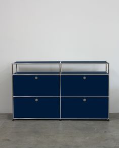 a blue dresser sitting on top of a cement floor next to a white wall with two drawers