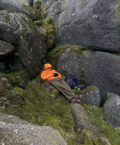 a man laying on top of a lush green field next to large rocks and moss