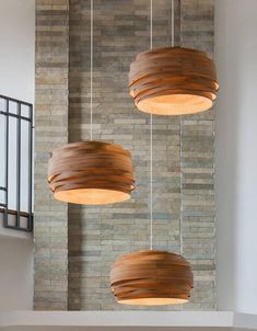 three wooden lights hanging from the ceiling in a room with brick wall and stairs behind them