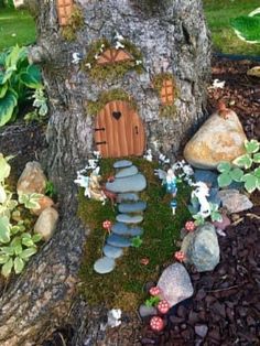 a fairy house built into the side of a tree in a garden with rocks and plants