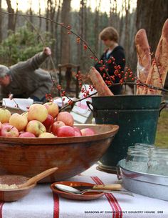 apples are in a wooden bowl on a table with other dishes and utensils