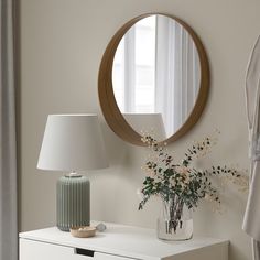 a white dresser topped with a vase filled with flowers and a round mirror above it