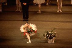 a ballerina sitting on the floor with flowers in front of her and other dancers behind her