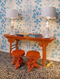 two orange stools sitting next to a wooden table with lamps on top of it