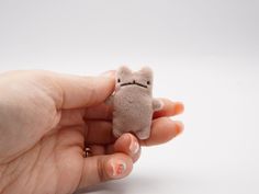 a hand holding a small stuffed animal in it's right hand, on a white background