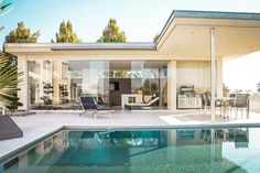 an outdoor swimming pool in front of a large house with glass walls and sliding doors