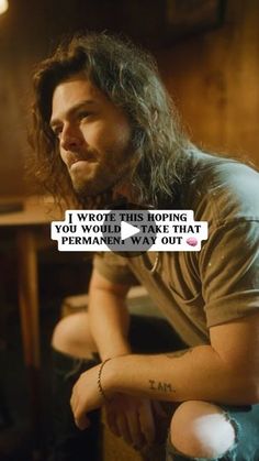 a man with long hair sitting in front of a table and looking off to the side