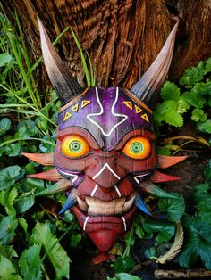 a colorful mask is sitting in the grass next to a tree and some green plants