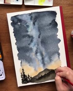 a watercolor painting of the night sky with stars and trees on it, next to some paintbrushes