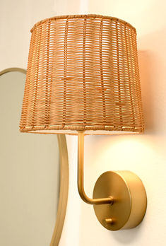 a wall light with a rattan shade on it and a mirror in the background