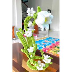 a green vase with white flowers sitting on a table in front of a colorful rug