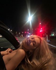 a woman sitting in the driver's seat of a car on a street at night