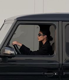 a woman sitting in the driver's seat of a black truck with her hand on the steering wheel