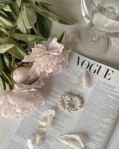 an open book with flowers and pearls on it next to a glass of wine,